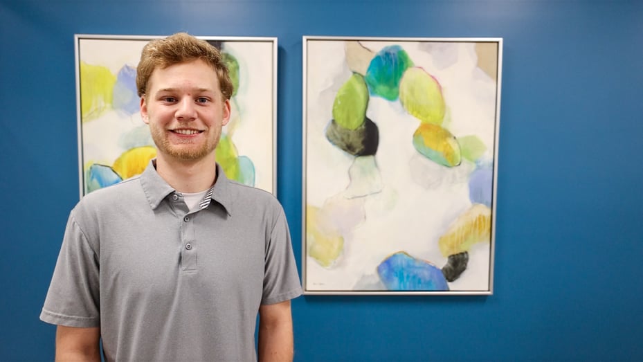 Blue intern Aidan Newett poses for a photo in front of artwork in the Indianapolis office