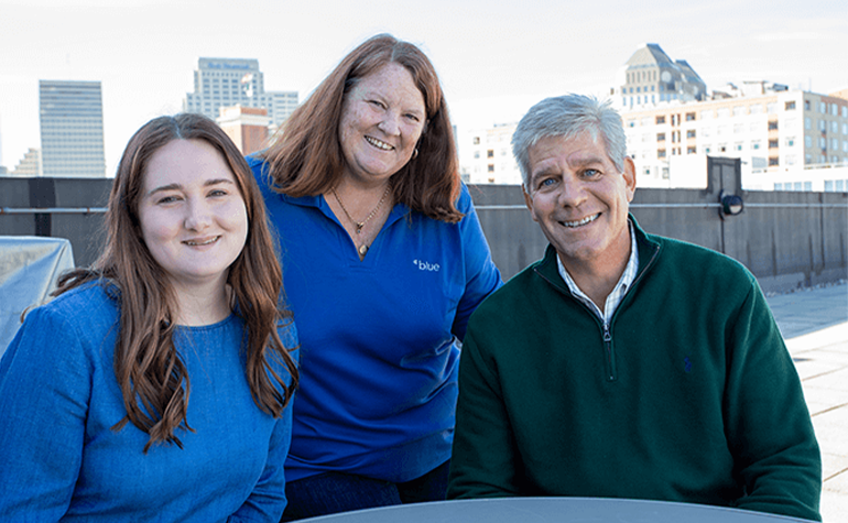 three coworkers posing for group photo on rooftop patio