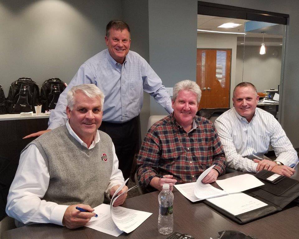 Four directors smile as they sign the papers to merge their firm with Blue's Columbus Ohio Office
