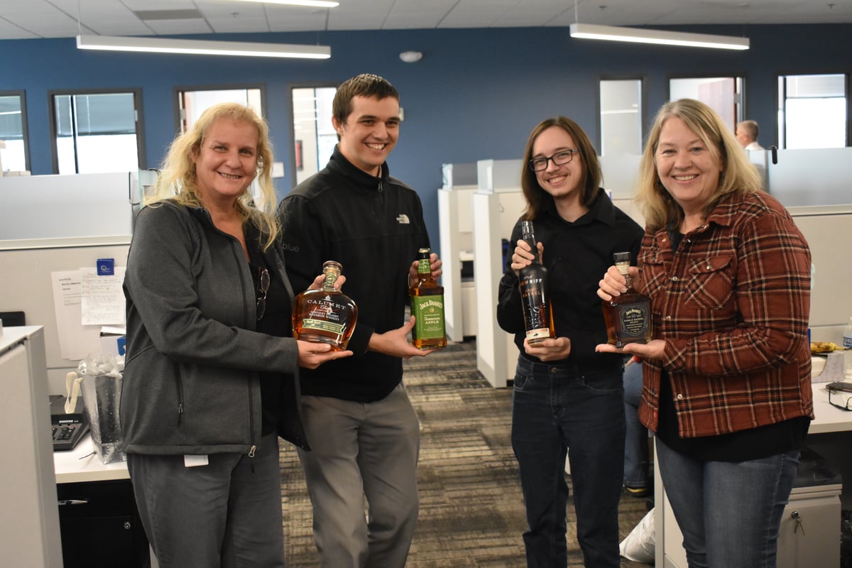 Four Columbus Ohio staff holding bottles of liquor they received during the Holiday Bottle Exchange