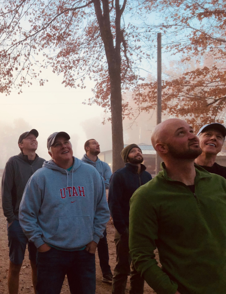 Members from the Building Leaders group watch in amazement as members are helped over the 20 foot wall at Camp Joy ropes course