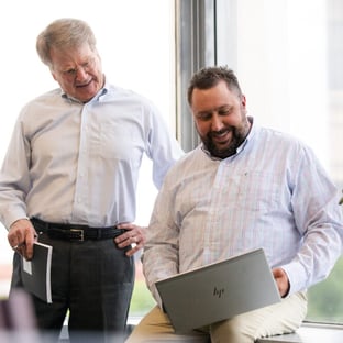 Two men looking down at laptop screen together